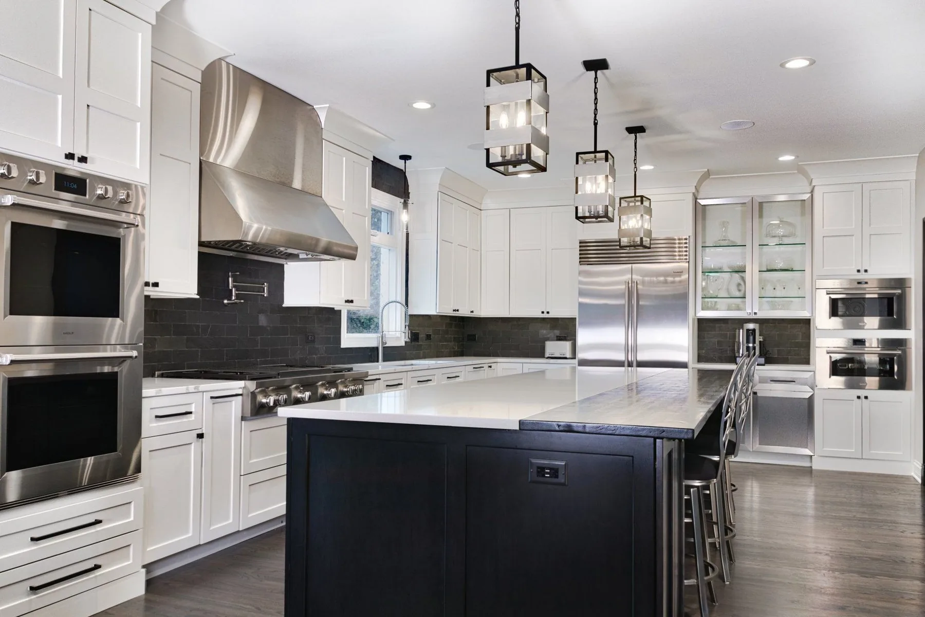 Remodeled white kitchen with a dark island and lantern pendants by Fredenhagen Remodel and Design