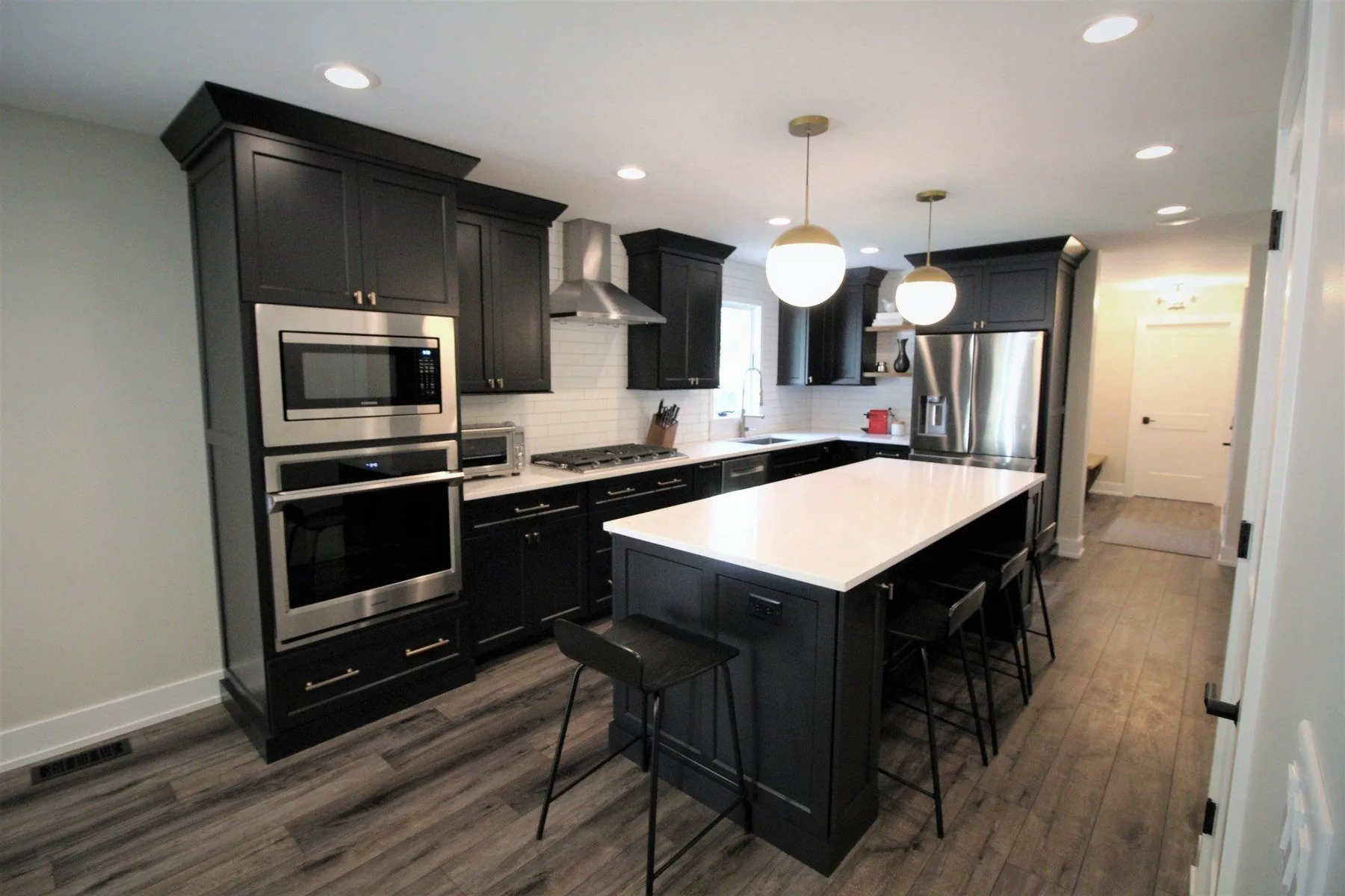 Completed kitchen remodel with black cabinetry and brass globe pendants